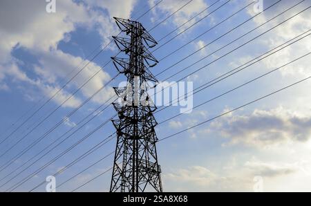 Nachmittagsansicht eines einzelnen hohen Übertragungsturms mit mehreren Stromleitungen, die sich von ihm unter teilweise bewölktem Himmel erstrecken Stockfoto