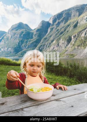 Sommer-Picknick in Norwegen - Kind Mädchen isst veganes Essen Salat Outdoor Familienreisen Urlaub Lifestyle, 4 Jahre altes Kind hat gesundes Frühstück mit Stockfoto