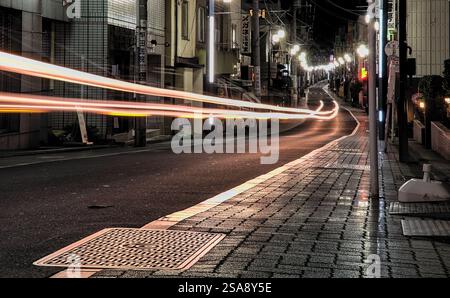 Nächtliche Sicht auf Lichtspuren, die durch eine lange Belichtung der Scheinwerfer eines Autos auf der Straße in Tokio, Japan, entstehen Stockfoto