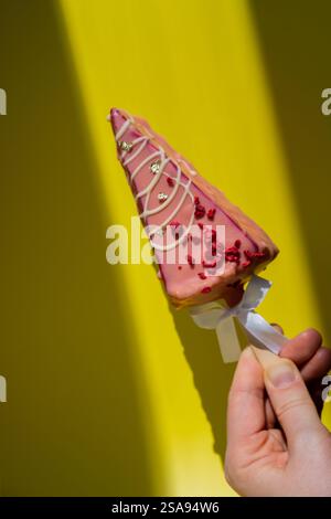 Neuer Look des trendigen Mini-Eis-Käsekuchens auf Stock in leuchtend rosa Farbe auf gelbem Hintergrund. Kopierraum Mustervorlage für Bäckerei Mini Dessert Coffee Shop. Kuchen zum Mitnehmen Süße Weihnachtsgeschenk-Idee eine Person Stockfoto