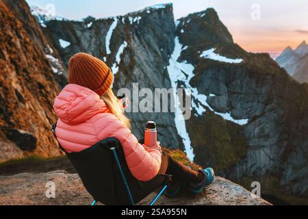 Frau, die in Norwegen reist, sitzt im Campingstuhl und trinkt Tee mit Thermos auf dem Berggipfel, Mädchen wandert allein auf den Lofoten-Inseln, Abenteuerurlaub Stockfoto