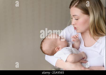 Eine liebevolle Mutter hält, schaukelnd, singt ein Lied, beruhigt ihr weinendes Baby. Eine Mutter schaut ihr Kind mit Liebe an. Das Konzept von Mutterschaft, Mutterschaftsurlaub Stockfoto