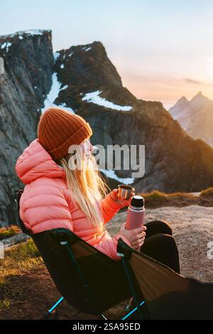 Frau chillt im Campingstuhl mit Thermos in den Bergen, die in Norwegen unterwegs sind Wandern im Freien, Mädchen trinkt heißen Kaffee, Abenteuer Urlaub Lebensstil Stockfoto
