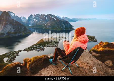 Frau, die sich im Campingstuhl mit Thermoskanne auf der Bergspitze Reinebringen entspannt, die in Norwegen unterwegs ist und im Freien wandert, Mädchen genießt die Lofoten-Inseln reine aeri Stockfoto