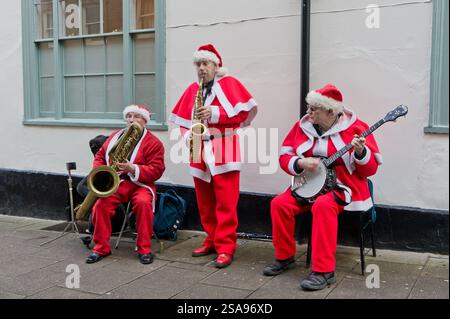 Drei Männer in Weihnachtsmannskostümen spielen Musik auf einem Weihnachtsmarkt in Bury St Edmunds, Suffolk, Großbritannien Stockfoto