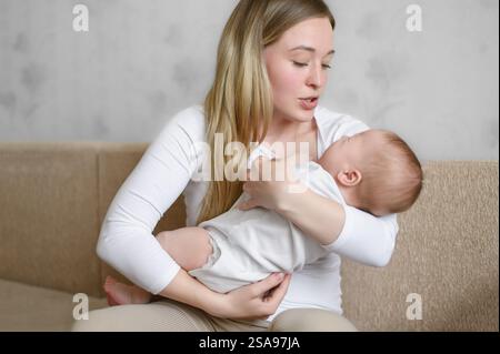 Eine liebevolle Mutter hält, schaukelnd, singt ein Lied, beruhigt ihr weinendes Baby. Eine Mutter schaut ihr Kind mit Liebe an. Das Konzept von Mutterschaft, Mutterschaftsurlaub Stockfoto