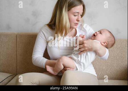 Eine liebevolle Mutter hält, schaukelt, singt ein Lied, beruhigt ihr weinendes Baby. Eine Mutter sieht ihr Kind mit Liebe an und beruhigt es. Das Konzept der Mutterschaft, MAT Stockfoto