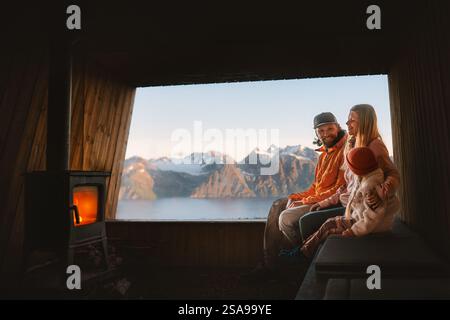 Familie genießt Kamin in gemütlicher Berghütte, Eltern reisen mit Kind in Norwegen - Mutter, Vater und Kind Tochter haben Spaß auf Urlaub Reise Stockfoto