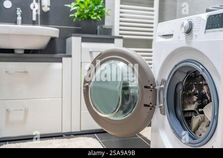 Waschmaschine mit offener Tür im modernen, weißen und grauen Badezimmer zu Hause Stockfoto