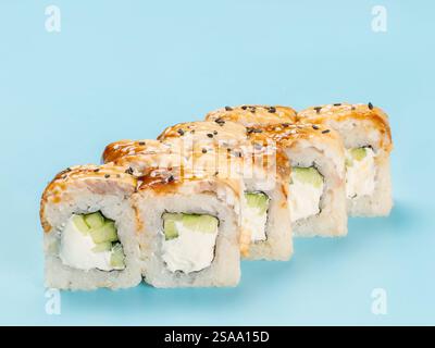 Studio-Fotografie von Philadelphia Roll mit samtigem Frischkäse und Gurke, gewickelt in perfekt gewürzten Sushi-Reis und frisch geräucherten Aal dekoriert mit schwarzen Sesamsamen. Isoliert auf hellblauem Hintergrund Stockfoto