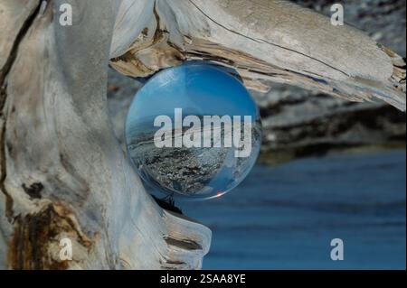 Kristallkugel auf Treibholz reflektiert den Strand und den Fluss Stockfoto