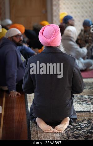 Ein Sikh-Mann in einem rosafarbenen Turban betet bei einem Morgengottesdienst an. Von hinten und in Queens, New York. Stockfoto