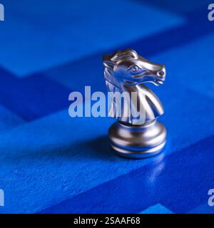 Markantes silbernes Schachritterstück auf einem blauen Schachbrett mit dezenten Highlights und Schatten. Stockfoto