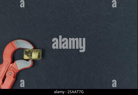 500 Euro-Münze, goldfarben in den Backen eines Rohrschlüssels. Währungen verlieren an Wert. Gold-Metallplatte, Abwertung Europa. Stockfoto