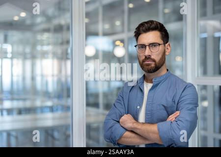 Porträt eines selbstbewussten seriösen Mannes am Arbeitsplatz im Büro. Geschäftsmann, der mit gekreuzten Armen in die Kamera schaut, erfolgreicher Finanzier Investor. Stockfoto