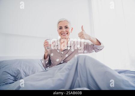 Eine ältere Frau im Pyjama lässt die Daumen hoch sitzen und das Morgenlicht genießen Stockfoto