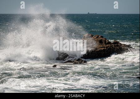 Mächtige Wellen krachen entlang der Küste auf Felsen und erzeugen einen nebeligen Sprühnebel. Stockfoto