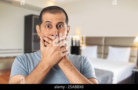 Schockierter Mann, der im Hotel seinen Mund mit Händen bedeckt Stockfoto