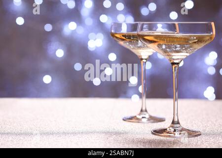 Champagner in Gläsern auf glänzender Oberfläche gegen verschwommenes Licht. Leerzeichen für Text Stockfoto