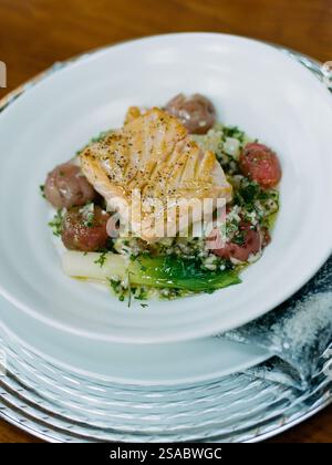 Ein wunderschön überzogenes gegrilltes Lachsfilet liegt auf gerösteten roten Kartoffeln und frischen Kräutern. Die Mahlzeit wird auf einem eleganten Esstisch serviert, in dem die Kul präsentiert wird Stockfoto
