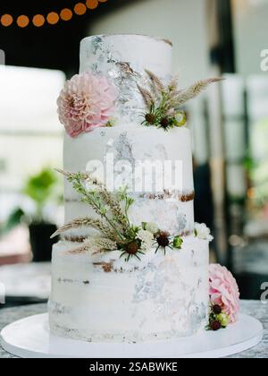 Eine wunderschön gestaltete dreistöckige Hochzeitstorte steht auf einem runden Sockel, dekoriert mit frischen Blumen und Grün, in einer stilvollen Rezeption Stockfoto