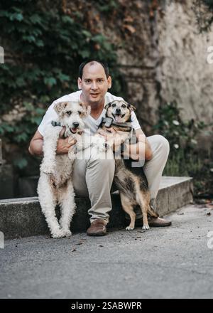 Ein Mann in einem Park umarmt zwei Hunde in einem Park. Das Porträt der Glatze zeigt bedingungslose Liebe zu seinen Haustieren. Ein Hund Fox Terrier Draht und die Stockfoto