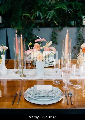 Ein wunderschön gestalteter Esstisch ist mit bunten Blumen, glühenden Kerzen und feinem Glasgeschirr geschmückt und schafft eine einladende Atmosphäre für einen gleichmäßigen Aufenthalt Stockfoto