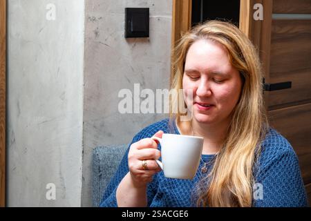 Frau genießt ein warmes Getränk, während sie sich in einer gemütlichen Inneneinrichtung entspannt Stockfoto