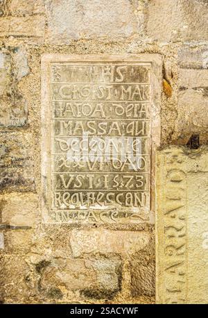 Ein verwitterter lateinischer Grabstein von 1573, auf einer alten Steinmauer montiert. Die Inschrift enthält Requiesant in Pace, was auf einen Begräbniszweck hindeutet. Stockfoto