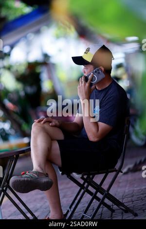 Mann, der auf einem Stuhl sitzt und ein Smartphone benutzt. Kommunikation. Ca Mau. Vietnam. Stockfoto