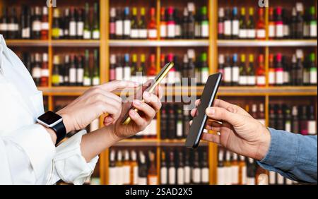 Menschen, die Smartphones vor dem Hintergrund von Weinflaschen in den Regalen im Geschäft benutzen. Mobile Zahlungstechnologien. Stockfoto