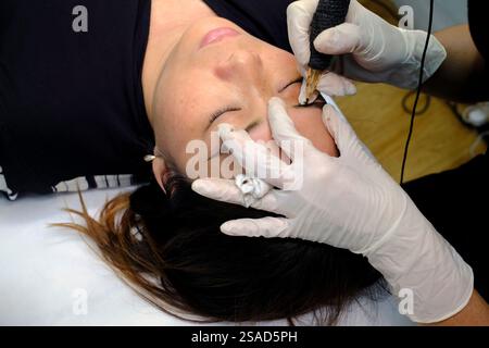 Kosmetikschrank und Schönheitsbehandlung. Kosmetikerin trägt permanente Tinte auf die Augenbrauen auf. Das Vorgehen bei permanentem Augenbrauen-Make-up. Ho-Chi-Minh-Stadt. Vietn Stockfoto