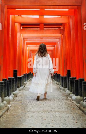 Wunderschöne Frau, die durch die roten Torii-Tore im Fushimi Inari-Schrein in Kyoto Japan läuft Stockfoto