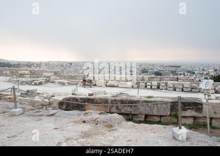 Ein Paar sitzt auf einer Steinbank auf der Westseite des Parthenon in der Akropolis, mit der Stadt Athen im Hintergrund. Griechenland. Stockfoto