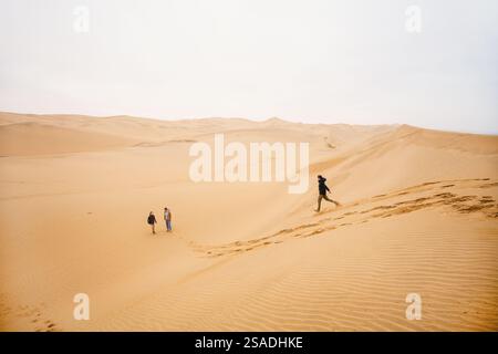 Familie mit Mutter und Kindern, die Spaß beim Ablaufen von der Sanddüne des Sandwich Harbour in Namibia haben Stockfoto