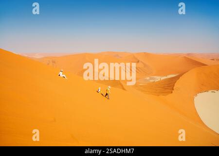 Familie mit Mutter und zwei Kindern, die Spaß beim Laufen und Rutschen von der berühmten roten Sanddüne Big Daddy in Sossusvlei Namibia haben Stockfoto