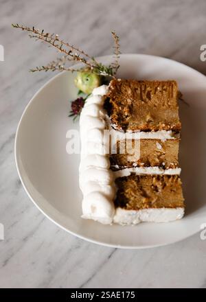 Ein wunderschön präsentiertes Stück Kuchen mit cremigem Zuckerguss ist garniert mit zartem Grün und Blumen. Der Kuchen sitzt auf einem sauberen W Stockfoto