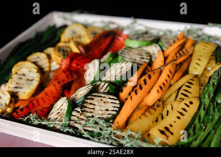 Eine lebendige Auswahl an gegrilltem Gemüse ist wunderschön in einem Holztablett angeordnet. Die farbenfrohe Auswahl umfasst Karotten, Zucchini, Spargel und Stockfoto