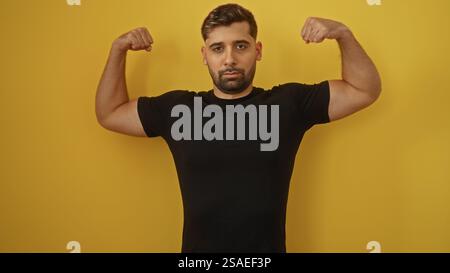 Mann beugt seine Muskeln in einer selbstbewussten Pose vor einem leuchtend gelben Hintergrund, der Stärke und Fitness zeigt. Stockfoto