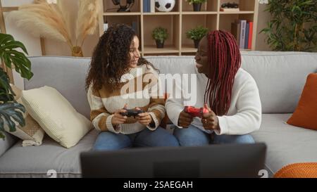 Zwei Freundinnen spielen zu Hause auf einer bequemen Couch in einem stilvollen Wohnzimmer Videospiele und genießen eine unterhaltsame und entspannte Atmosphäre. Stockfoto