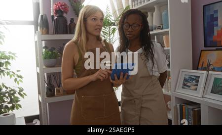 Frauen in Schürzen, die in einem Wohnhaus arbeiten und Informationen auf einem Tablet diskutieren, das von dekorativen Gegenständen und Pflanzen umgeben ist Stockfoto