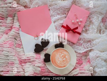 Frühstück zum Valentinstag. Komposition mit einer Tasse pinken Latte, Geschenkbox, Schokoladenherzen, Ehering und Grußkarte. Modell. Stockfoto