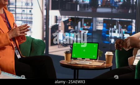 Ein multiethnisches Expertenteam teilt neben dem Chroma Key Screen Erkenntnisse und bewertet die Leistungskennzahlen des Unternehmens und der Mitarbeiter. Weibliche Führungskräfte, die Daten-Infografiken analysieren. Kamera A.. Stockfoto