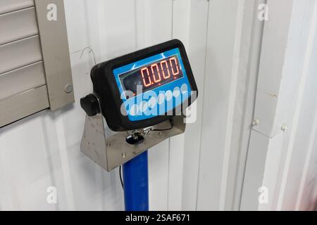 Eine digitale Waage ist auf einem blauen Pfosten in einer Lagereinrichtung montiert. Auf dem Display wird Null angezeigt, was darauf hinweist, dass kein Gewicht erkannt wurde. Die Umwelt i Stockfoto