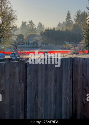 Hinterleuchteter orangefarbener Kunststoffzaun mit „Hirschzaun“ davor. Im Gegensatz zu permanenten vertikalen Holzdielen im Vordergrund Stockfoto