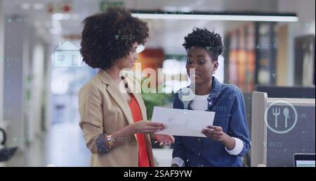 Bild von Diagramm und Datenverarbeitung über birassische Kolleginnen, die im Büro sprechen Stockfoto