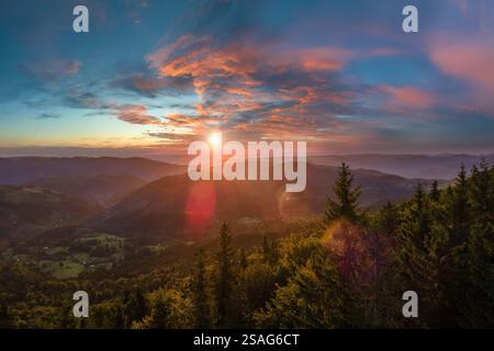 Wunderschöne Naturlandschaft. Aus der Vogelperspektive auf den farbenfrohen Sonnenuntergang in wilden Bergen. Dunkler Kiefernwald beleuchtet mit heller untergehender Sonne Stockfoto