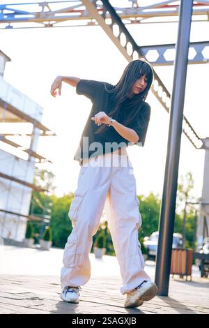 Die Tänzerin führt während des Sonnenuntergangs an einem urbanen Ort im Freien ausdrucksstarke Bewegungen in einem stilvollen Outfit durch Stockfoto