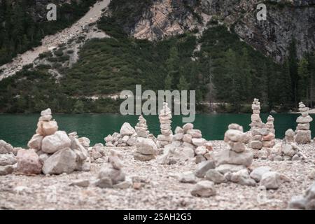 Eine ruhige Naturszene mit einer Sammlung ausgewogener steinhügel an einem felsigen Ufer, mit einem unberührten türkisfarbenen Bergsee und üppigem Grün Stockfoto