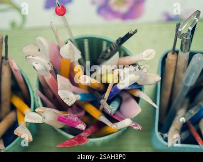Werkzeuge des Keramikkünstlers. Draufsicht auf Stapel, Jakobsmuscheln, Bleistifte und Pinsel, die sich in einem speziellen Becher befinden. Stockfoto